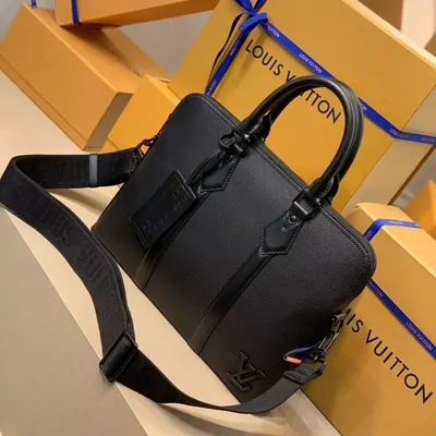 A black leather briefcase-style bag with a shoulder strap resting on its packaging boxes